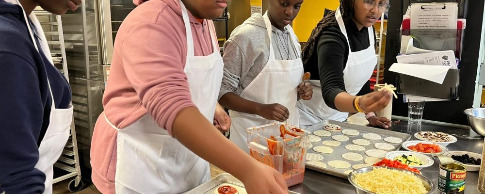 Volunteers making pizza and adding toppings to dough.